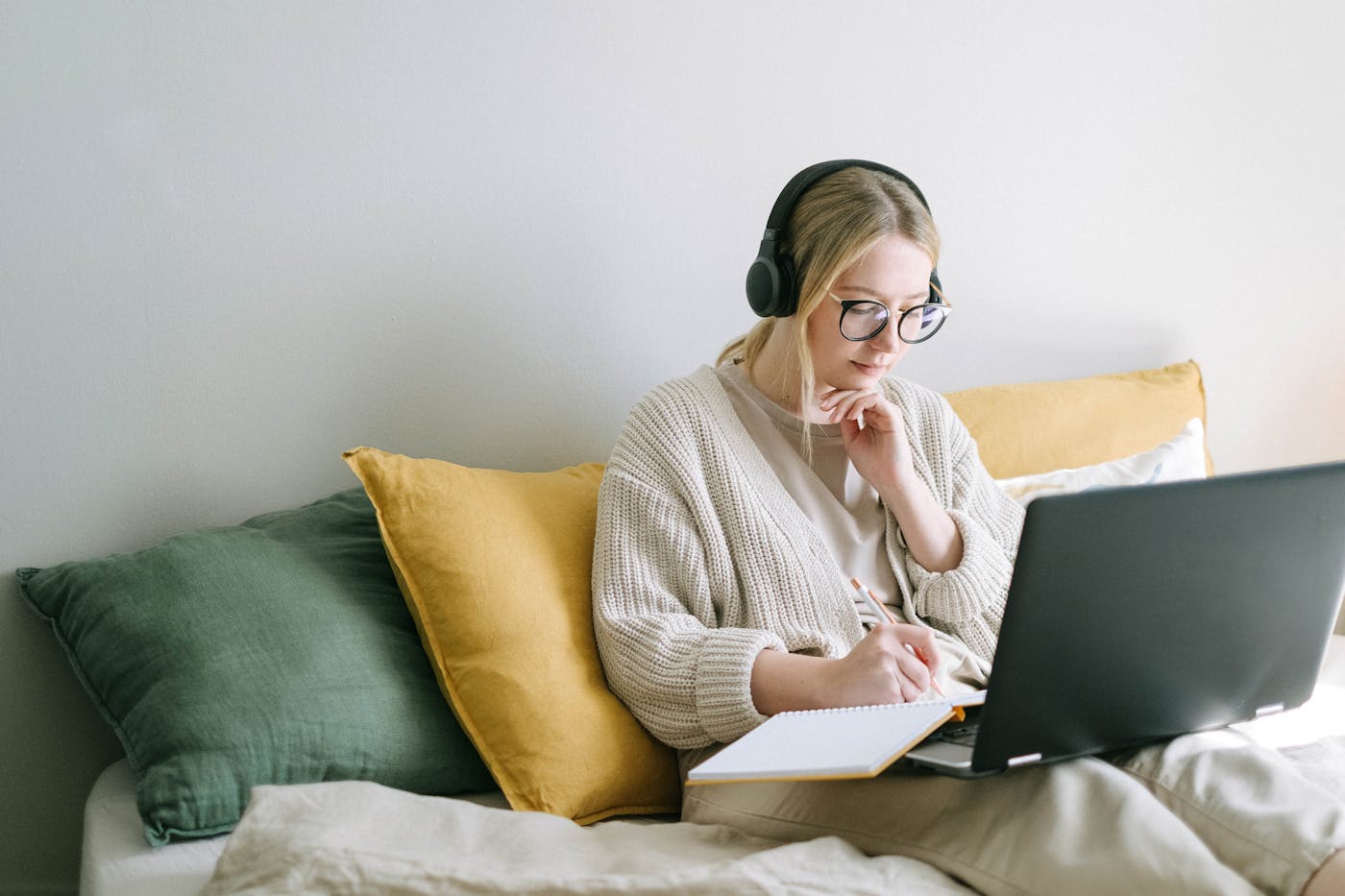 A woman in headphones organizing her notes beside a laptop at home